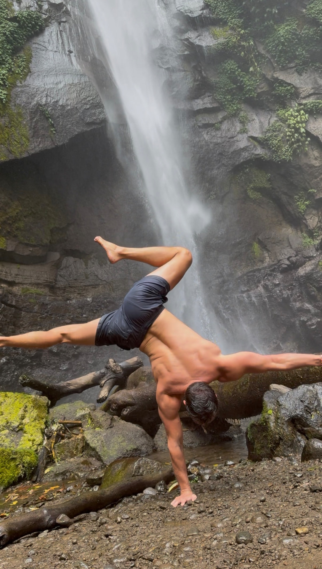 Romain performing a one-arm handstand in front of a waterfall